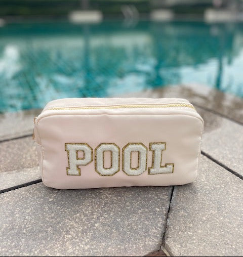 Cream pouch with 'POOL' text on a stone surface near a pool.